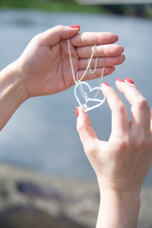 Malli pitää käsissään Riia Valvimon suunniteleman Rovaniemi aiheisen korumalliston Rovaniemi LOVE:n Joki-hopeista kaulakorua, jossa sydämen mallinen muotoilultaan ilmava, mutta kookas riipus ja kiiltävä pinta.