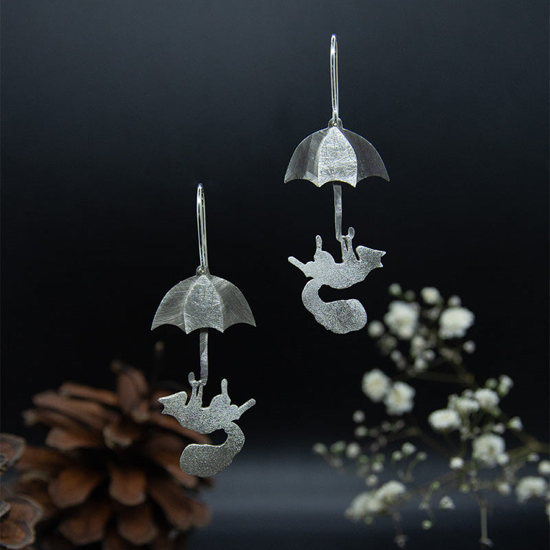 Hopeiset orava-aiheiset korvakorut koukkumekanismilla. Korussa orava näyttää leijailevan sateenvarjon kanssa.