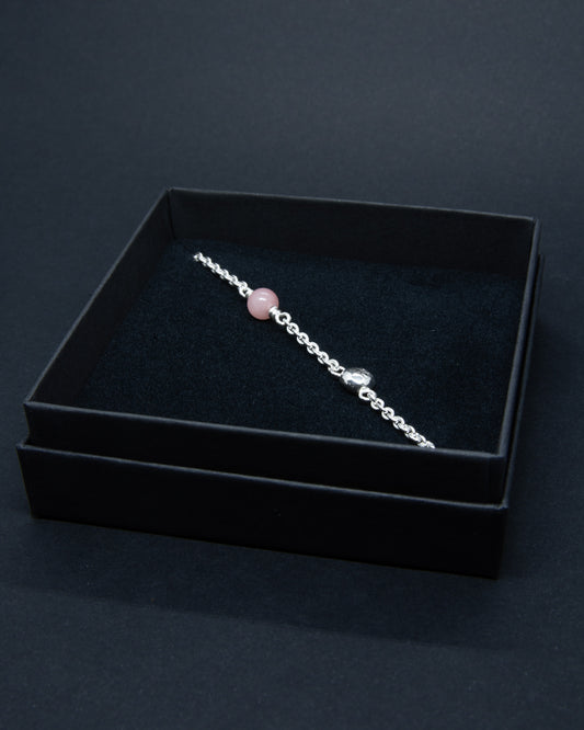 Hopeinen naisten rannekoru vaaleanpunaisella kivihelmellä ja käsityönä tehdyllä yksityiskohdalla. Koru on mustassa pahvisessa korurasiassa.