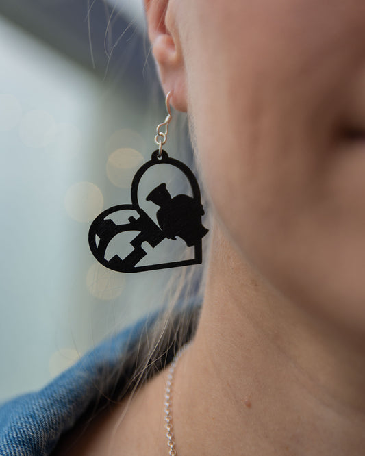 Musta Oulu-aiheinen vanerikorvakoru, josta voi tunnistaa Toripoliisin ja Oulun Kauppahjallin.