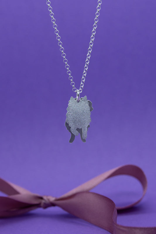 Hopeinen pieni ja mattapintainen suomenlapinkoiraa esittävä kaksiosainen riipus hopeaketjussa. Lähikuva riipuksesta.