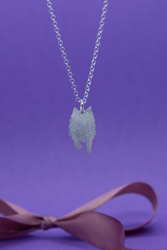 Hopeinen pieni ja mattapintainen suomenlapinkoiraa esittävä riipus hopeaketjussa. Lähikuva riipuksesta.