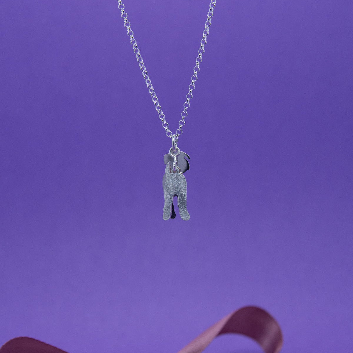 Leikkisä hopeakaulakoru kaksiosaisella riipuksella kuvattu takaa päin. Riipus esittää suursnautseria. Riipus on takaa mattapintainen. Sisäpinnat kiiltävät. Kaulakorussa on siro papuketju.