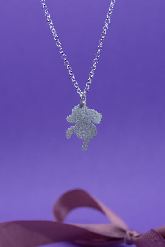 Mattapintainen villakoiran siluettia esittävä hopeariipus papuketjussa. Lähikuva riipuksesta.