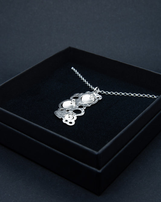 Kiiltäväksi käsitelty hopeakaulakoru, jossa on kolme mattapintaista ja kuperaa helaa korun keskiössä kauniina yksityiskohtina.