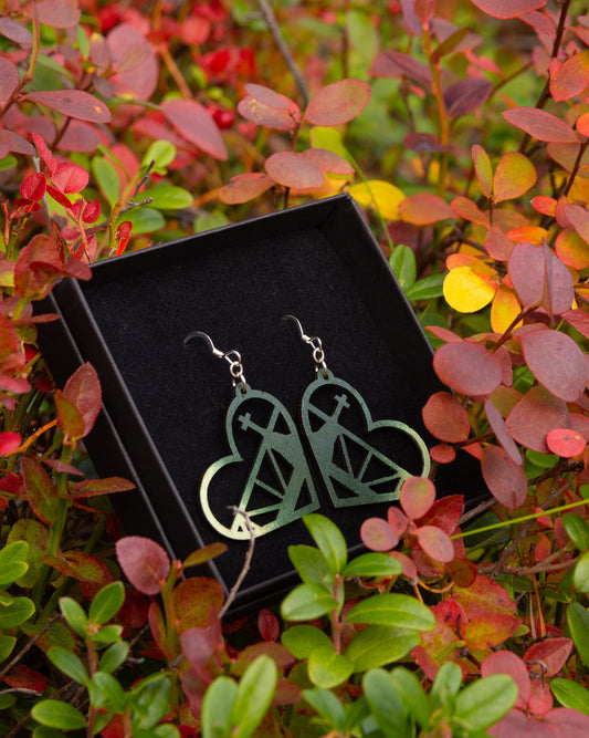 Vihreän sävyiset vanerikorvakorut, joista voi tunnistaa Rovaniemen kirkon ristin ja vanhan sillan siluetin. Korujen ulkokehä on sydämen muotoinen.