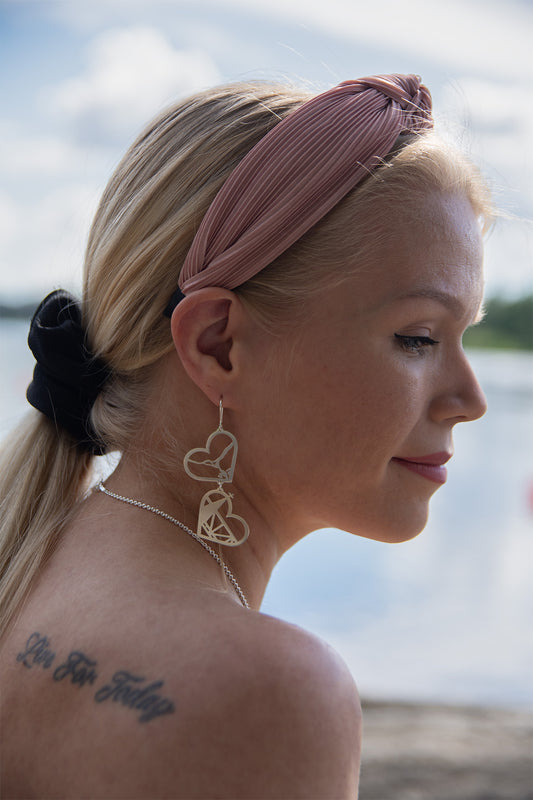 Sivusta otettu kasvokuva vaaleahiuksisesta mallista, jolla korvissaan hopeiset Rovaniemi LOVE - korumalliston kaksiosaiset, näyttävät korvakorut. Korvakorussa kaksi alekkain roikkuvaa sydänmuotoa joista voi tunnistaa Kemi- ja Ounasjoen, Rovaniemen Kirkon ja vanhan sillan.