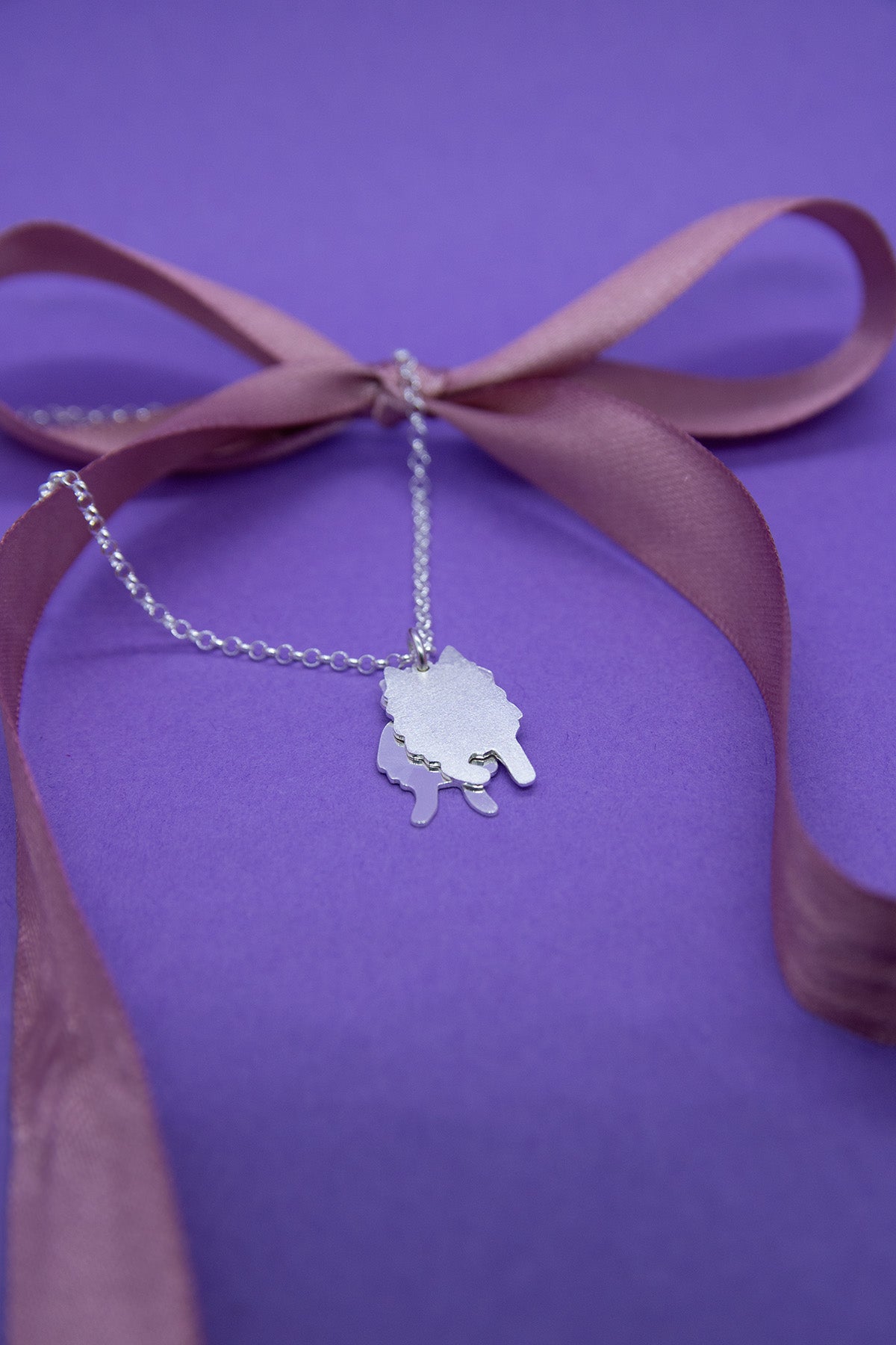 Hopeinen pieni ja mattapintainen suomenlapinkoiraa esittävä kaksiosainen riipus hopeaketjussa. Koru kuvattuna pöydälle asetettuna.