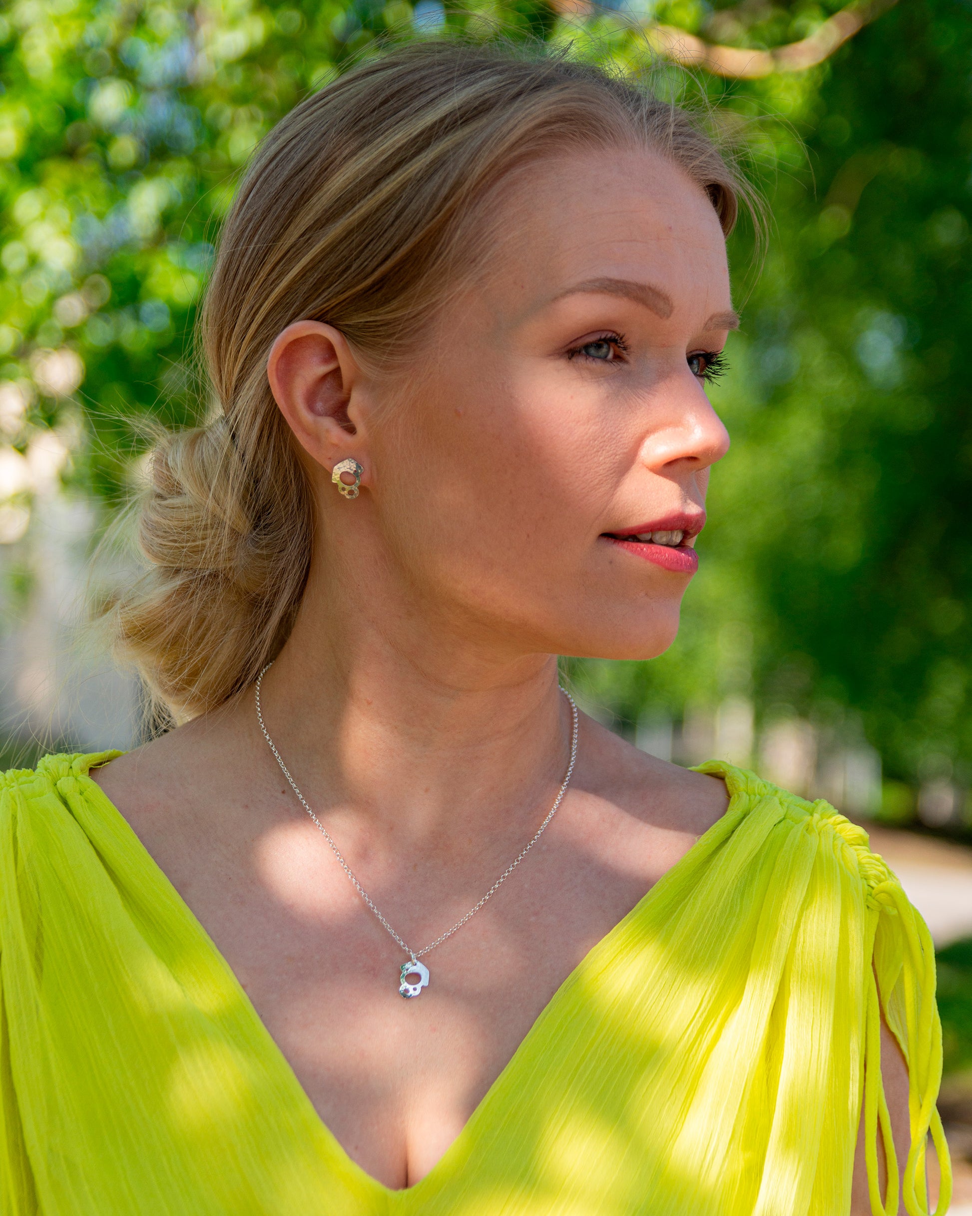 Naismallilla yllä sievät kiiltävät hopeakorvakorut, joissa on vasaroitu pinta, ilmava muotoilu ja epäsäännöllinen ulkokehä.