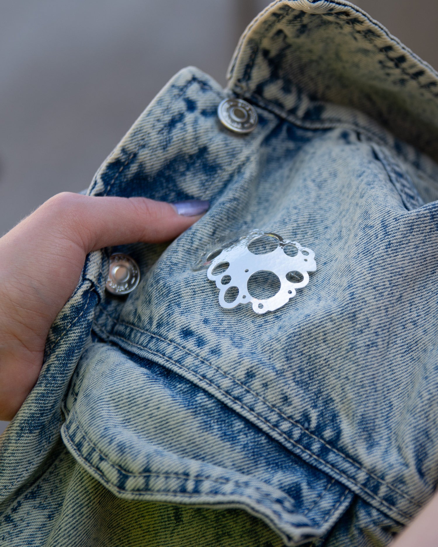 Hopeinen näyttävä Rannalla-malliston rintaneula kiinnitetty farkkutakin rintapieleen.