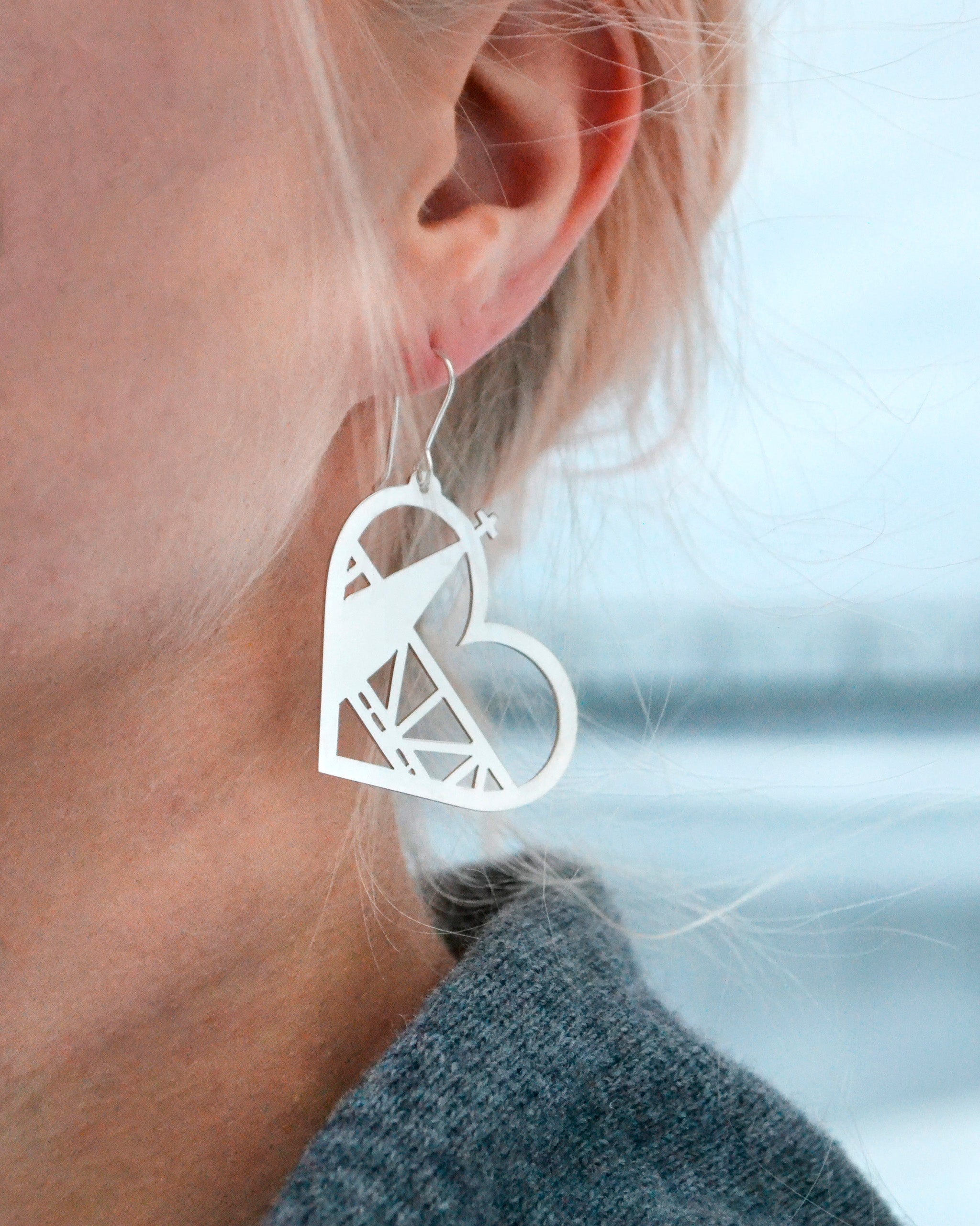 Rovaniemi LOVE -malliston sydämen muotoinen kiiltävä Kirkko-hopeakorvakoru mallin päällä vasemmassa korvassa. Ulkona otettu lähikuva.